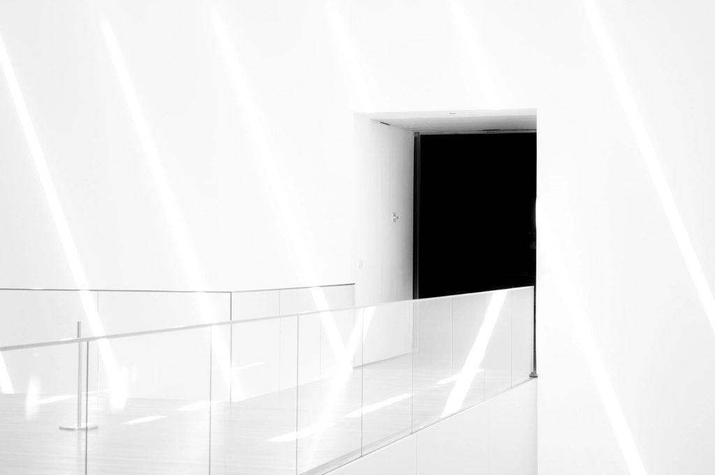 Minimal white interior landing with a flush dark door opening and glass balustrade