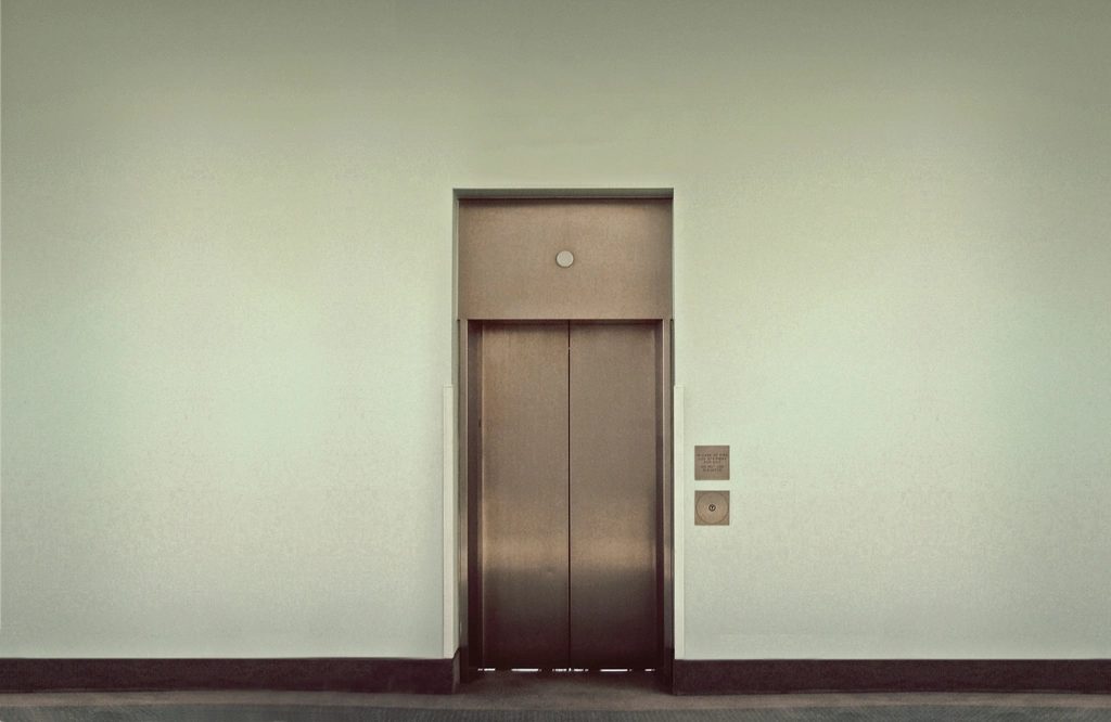 Flush metal-faced door set in a plain wall with concealed frame and call plate