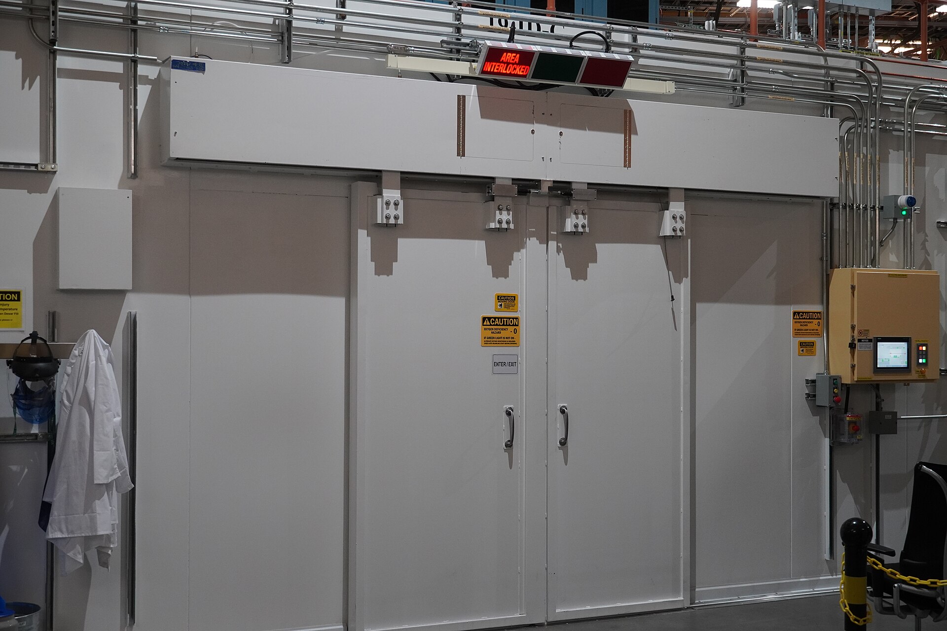 Large paired sliding doors sealing a controlled-environment chamber with interlock control panel