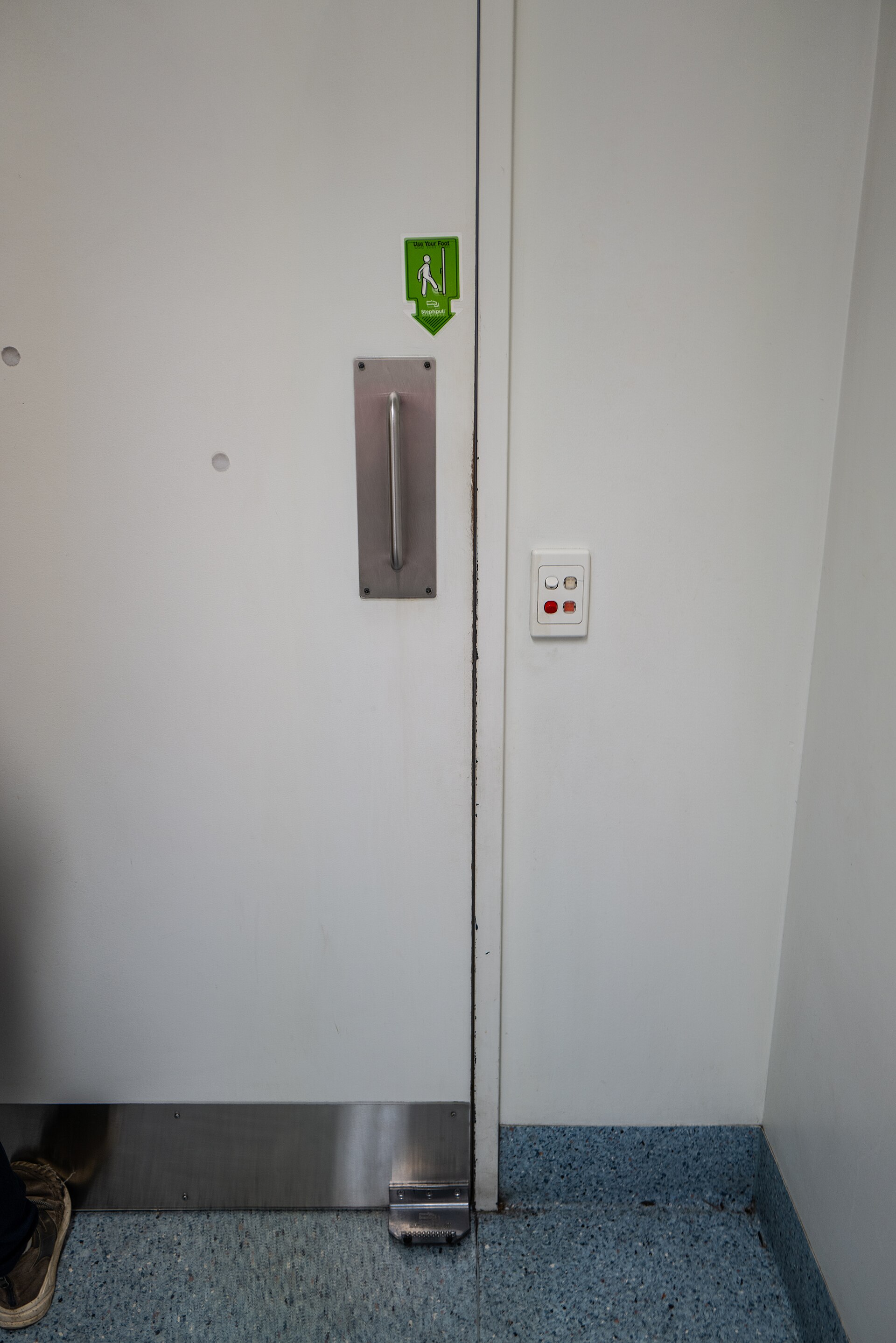 Hospital door leaf fitted with a hands-free foot pull at the base and a stainless kick plate