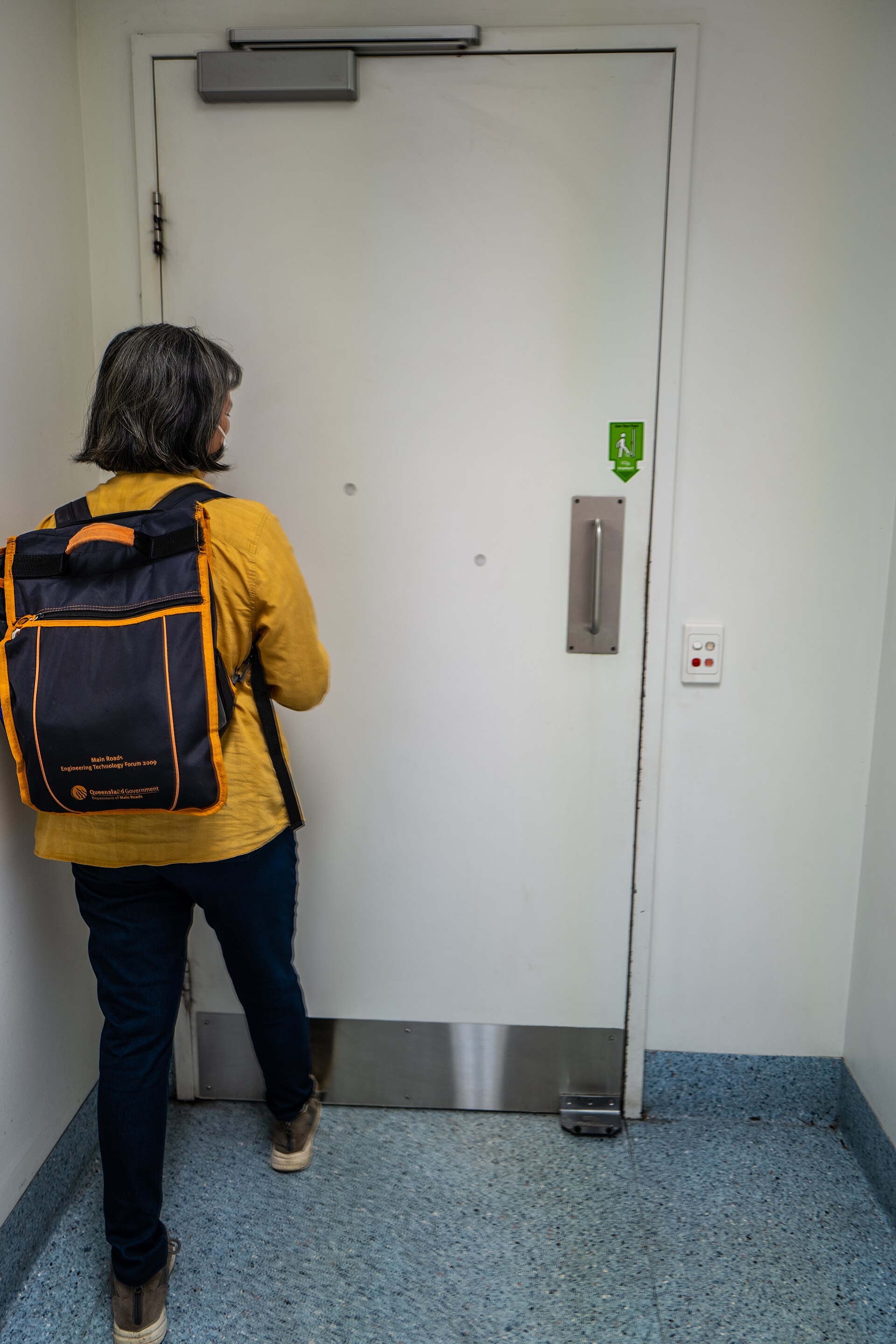 Person operating a hospital door with a hands-free foot pull, closer visible at the door head