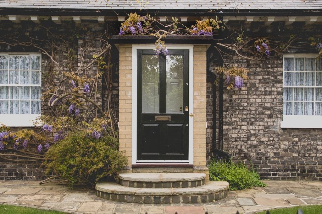 Dark glazed front door in a brick house facade framed by climbing planting