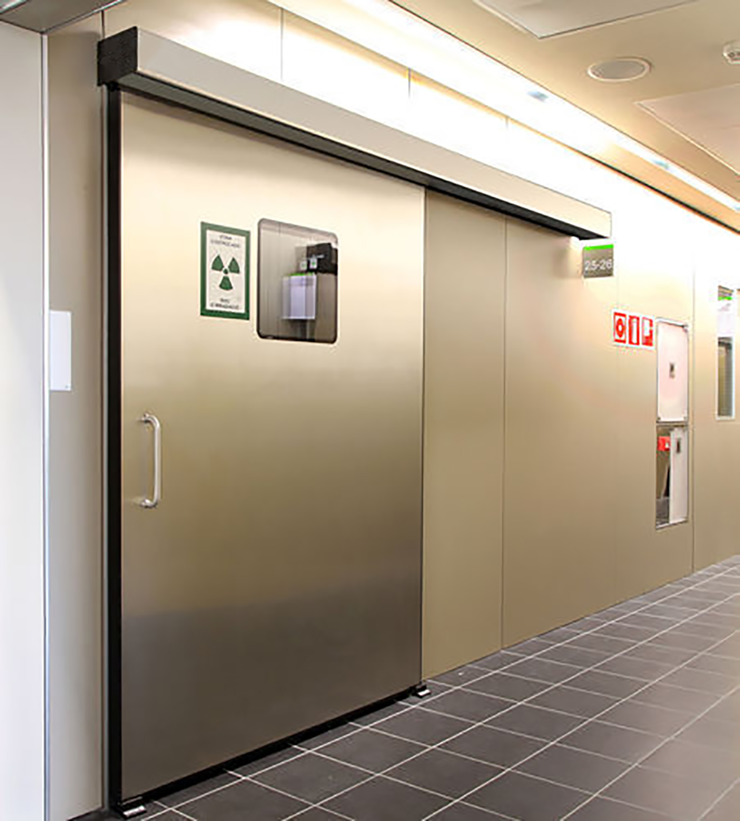 Hermetically sealed sliding door leaf with stainless pull and radiation warning sign in a clinical corridor