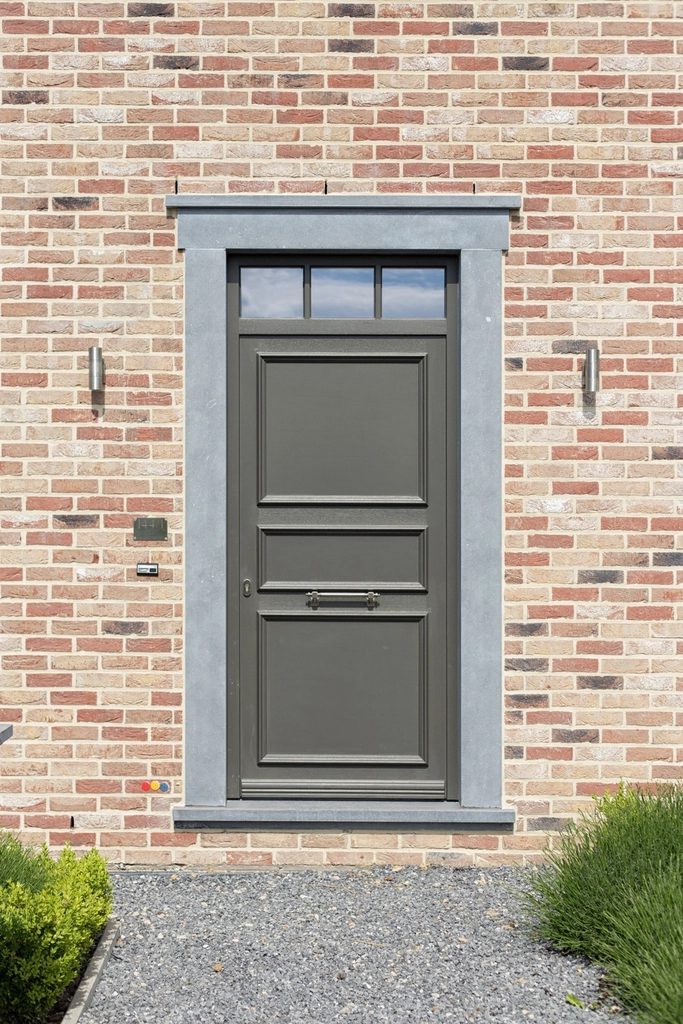 Grey panelled entry door set into a brick facade with a gravel threshold