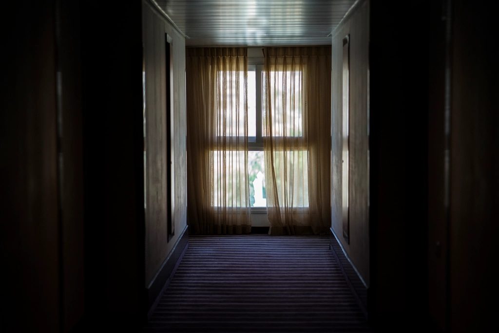 Dim hotel corridor leading to a glazed door with daylight beyond